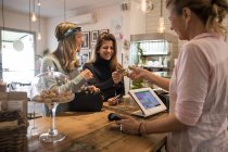 Zwei Freundinnen stehen am Schalter im Café und geben der Verkäuferin die Kreditkarte zur Bezahlung — Stockfoto