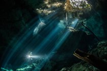 Plongeur plongeur dans une rivière souterraine (cenote) avec des rayons du soleil et des formations rocheuses, Tulum, Quintana Roo, Mexique — Photo de stock