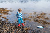 Ragazzo al bordo del fiordo d'acqua che gioca con la barca giocattolo, Aure, More og Romsdal, Norvegia — Foto stock