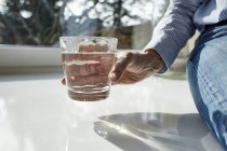 Donna anziana in possesso di un bicchiere d'acqua, primo piano vista parziale — Foto stock