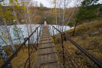 Rear view of small group of hikers walking over river footbridge, Kislokan, Evenk, Russia — Stock Photo