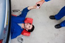 Mechanic handing coffee to colleague on floor — Stock Photo