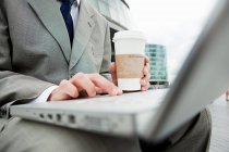Бізнесмен з кавою, що працює на ноутбуці на вулиці — стокове фото