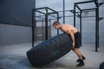 Man exercising in gymnasium, lifting tire — Stock Photo