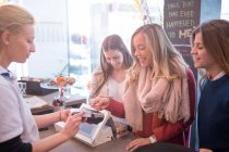 Amigos do sexo feminino em pé no balcão no café, pagando com cartão de crédito — Fotografia de Stock