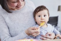 Закрыть мать, кормящую ложкой маленькую дочку — стоковое фото