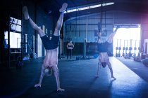 Three people exercising in gym, two men doing handstand walks — Stock Photo