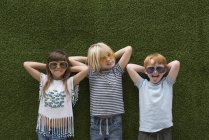 Niños frente a la pared de césped artificial en gafas de sol - foto de stock