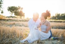 Couple sitting face to face and smiling in field — Stock Photo