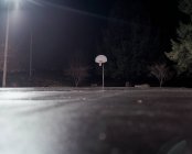 Cancha de baloncesto vacía con aro de baloncesto por la noche, a nivel de superficie - foto de stock