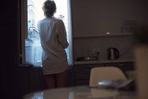 Rückansicht einer Frau im Hemd, die in den Kühlschrank blickt — Stockfoto