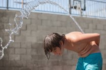 Seitenansicht eines Jungen, der Wasser über den Rücken spritzt — Stockfoto