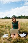 Jovem mulher usando laptop no meio do campo — Fotografia de Stock