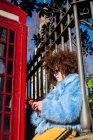 Mujer por mensajes de texto tradicionales de la cabina de teléfono rojo en el teléfono inteligente - foto de stock