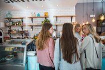 Three female friends, standing at counter in cafe, rear view — Stock Photo