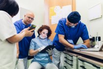 Dentistas em consultório odontológico olhando para tablet digital, laptop e smartphone — Fotografia de Stock