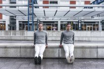 Junge männliche Zwillinge machen rückwärts Liegestütze gegen Mauer in der Stadt — Stockfoto