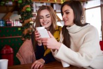 Молодые женщины улыбаются через смс на мобильном телефоне — стоковое фото