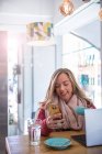 Женщина с использованием смартфона и проведение кофе Кубок, сидя в кафе — стоковое фото