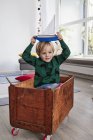 Молодий хлопець сидить в іграшковій коробці і тримає іграшковий човен на голові — стокове фото
