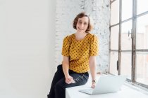 Портрет бізнес-леді, що сидить на підвіконні з ноутбуком — стокове фото