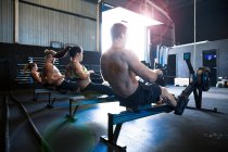 Grupo de pessoas que se exercitam no ginásio, usando máquinas de remo, visão traseira — Fotografia de Stock