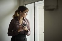 Бізнес-леді тримає смартфон і дивиться з вікна — стокове фото