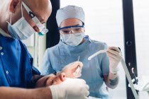 Стоматолог и зубная медсестра проводят стоматологическую процедуру на пациенте-мужчине крупным планом — стоковое фото