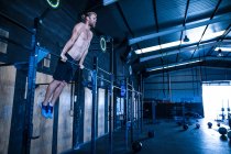 Man exercising in gymnasium, using pull up bars — Stock Photo