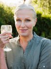 Portrait of woman holding glass of white wine and looking at camera — Stock Photo