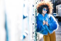 Portrait of woman with afro hair wearing fur coat against wall — Stock Photo