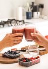 Cropped image of friends clinking with glasses of smoothies at home — Stock Photo