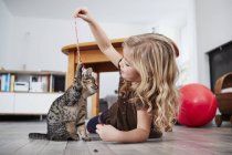 Young girl lying on floor and playing with cat — Stock Photo