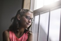 Молода дівчина в окулярах дивиться з вікна — стокове фото