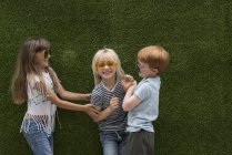 Niños frente a la pared de césped artificial jugando en cosquillas - foto de stock