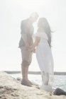Casal em pé sobre rochas costeiras, de mãos dadas, face a face, Seal Beach, Califórnia, EUA — Fotografia de Stock