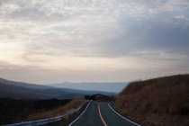 Strada vuota con tramonto al cielo nuvoloso e montagne all'orizzonte — Foto stock