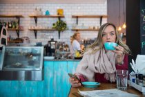 Женщина сидит в кафе, держит смартфон, пьет кофе — стоковое фото