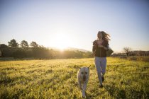 Young woman running across field with dog — Stock Photo