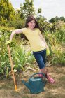Portrait of girl in garden with rake and watering can — Stock Photo