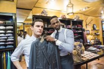 Tailor holding bespoke suit jacket against customer in tailor shop — Stock Photo