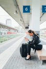 Жінка сидить на залізничній платформі і використовує смартфон — стокове фото