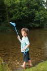 Мальчик держит рыболовные сети у реки — стоковое фото