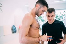 Freunde im Fitnessstudio schauen gemeinsam aufs Smartphone — Stockfoto