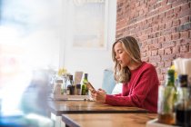 Вид сбоку женщины, смотрящей на смартфон в кафе — стоковое фото