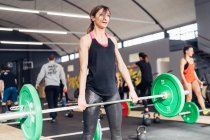 Levantamiento de pesas de mujer joven con barra en el gimnasio - foto de stock