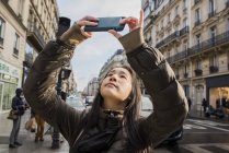 Mujer joven asiática tomando fotos de teléfonos inteligentes en la calle de la ciudad, París, Francia - foto de stock
