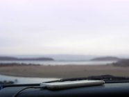 Смартфон на приборной панели автомобиля, вид на побережье через лобовое стекло автомобиля, Брули, Австралия — стоковое фото