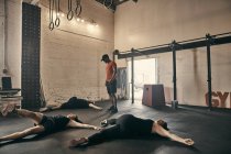 Instrutor de ginástica supervisionando pessoas fazendo exercícios no chão no ginásio — Fotografia de Stock