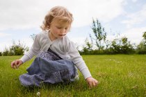 Girl picking daisies on green field — Stock Photo